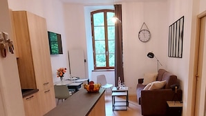 A modern living space with a kitchen area, a dining table, a sofa, and a large window providing natural light. - Magnificent 3 stars flat (Aulus-les-Bains)