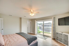 A bedroom with a bed, a ceiling fan, a TV, and a view of a water body through a sliding glass door. - Palm Coast Gem w/ Dock & Hot Tub! (Palm Coast)