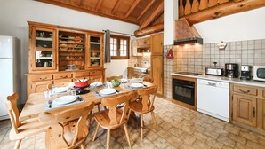 A wooden dining table with chairs, a kitchen with wooden cabinets, a tiled backsplash, and a ceiling with exposed beams. - Chalet "Eterlou" with Mountain View, Balcony and Wi-Fi (Lanslebourg Mont-Cenis)