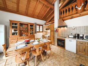 Ein Holzesstisch mit Stühlen, eine Küche mit Holzausbau, einer Fliesenküchenrückwand und einer Decke mit freiliegenden Balken.