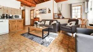 A cozy living room with a sofa, armchairs, and a coffee table. There's a kitchen area with appliances and wooden cabinets. - Chalet "Eterlou" with Mountain View, Balcony and Wi-Fi (Lanslebourg Mont-Cenis)