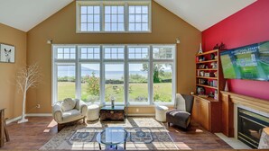 A living room with a large window, a fireplace, and a bookshelf. - Waterfront Bellingham Bliss: Steps to Beach! (Bellingham)