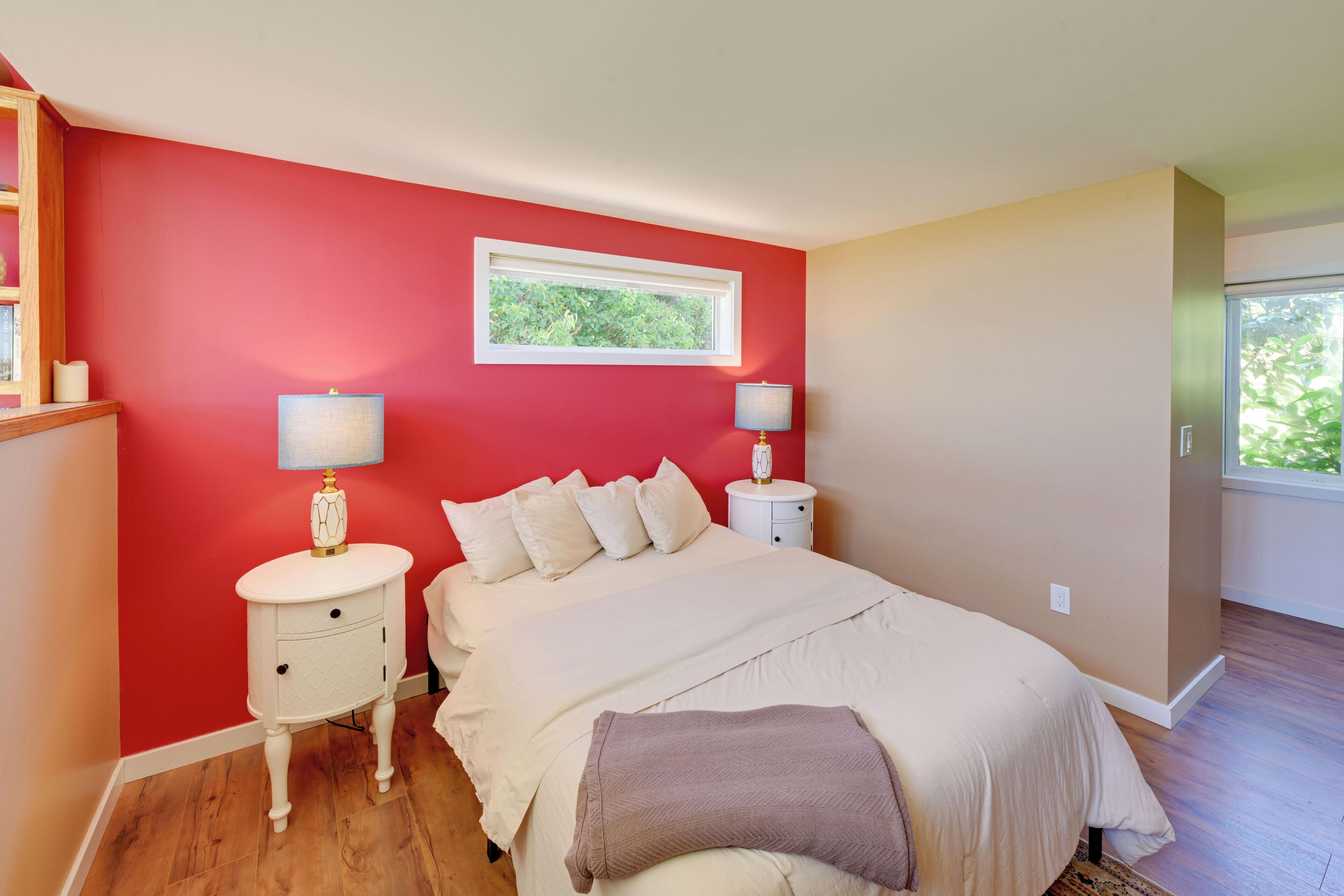A bedroom with a large bed, bedside lamps, a window, and a wooden floor.