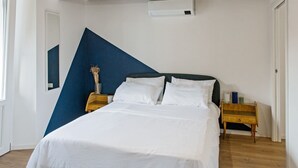 A bedroom with a bed, a nightstand, a wall-mounted air conditioner, and a window.