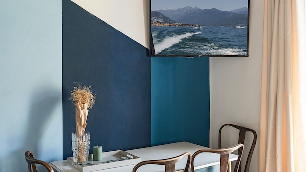 A dining area with a table, chairs, a vase with dried plants, and a framed picture of a coastal scene.