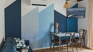 A dining area with a table and chairs, a sofa with a dog, and a wall with geometric patterns.