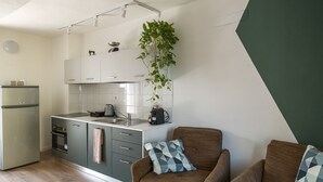 A compact kitchen with a refrigerator, stove, and sink. A hanging plant adds greenery.