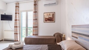 Habitación de hotel con dos camas, televisión, aire acondicionado, ventana con cortinas y un cuadro en la pared.