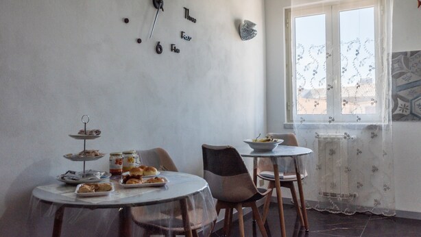 Un coin repas avec une table mise pour le repas, des chaises, une horloge au mur et une fenêtre donnant sur un paysage.