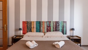 Une chambre d’hôtel avec un grand lit, deux tables de chevet, une porte en bois et une peinture abstraite aux couleurs vives accrochée au mur.