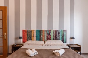 A hotel room with a large bed, two bedside tables, a wooden door, and a colorful abstract painting on the wall.