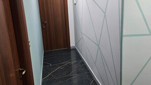 Un couloir avec une porte en bois, un mur bleu clair et un autre mur orné d’un motif géométrique.