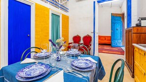 Un coin repas avec une table dressée pour deux personnes, des chaises et un espace cuisine comprenant des placards et un évier.