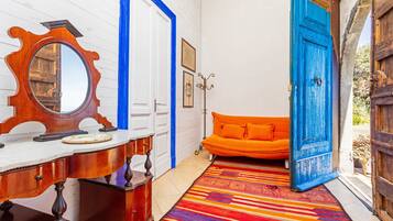Ein Zimmer mit einem hölzernen Schminktisch, einem farbenfrohen Streifen Teppich, einem orangefarbenen Sofa und einer blauen Tür.