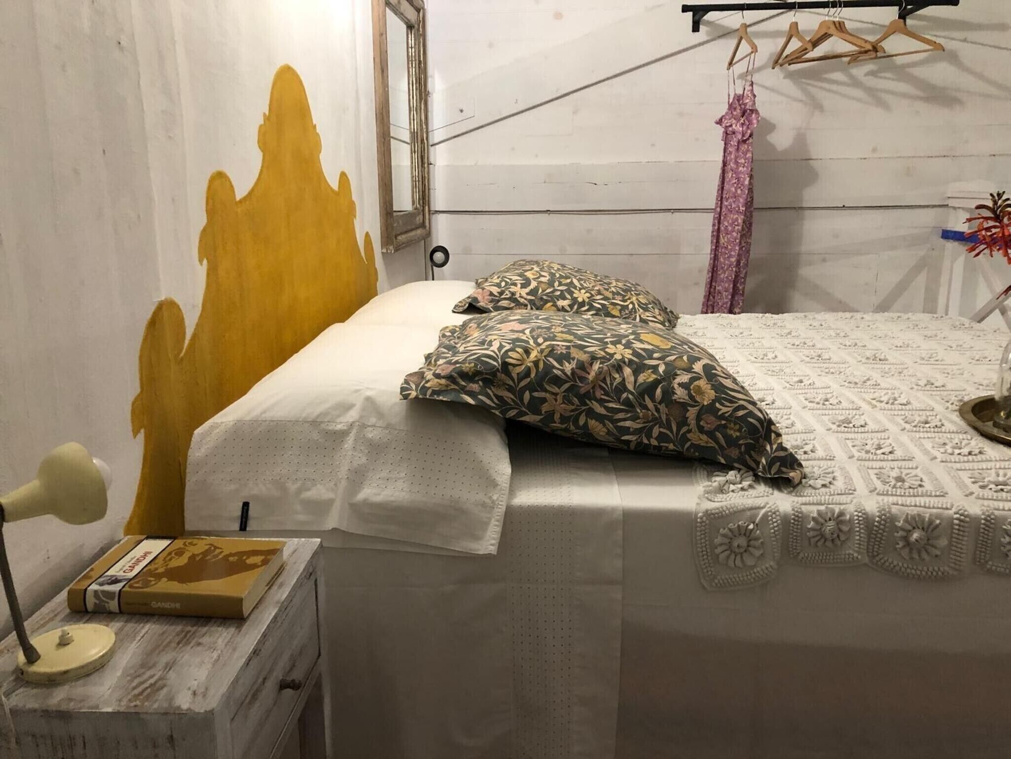 Een bed met een witte dekbedovertrek, twee kussens met een patroon, een klein nachtkastje met een lamp en een boek.