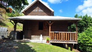 A wooden cabin with a porch, a stone wall, and a white vase.