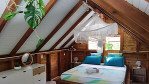 A bedroom with a bed, bedside tables, a nightstand, a mirror, and a hanging plant.