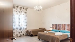 A bedroom with two beds, a chandelier, floral curtains, and a patterned wall. - Room 'Stanza Fiore' with Wi-Fi and Air Conditioning (Agrigento)