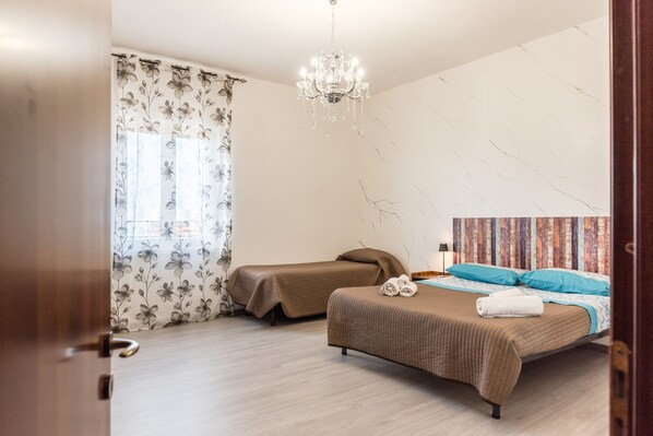 Une chambre avec deux lits, un lustre, des rideaux à motifs floraux et un papier peint à motifs.