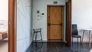 A hallway with a wooden door, a black chair, a small table, and a wall-mounted phone. - Room 'Stanza Fiore' with Wi-Fi and Air Conditioning (Agrigento)