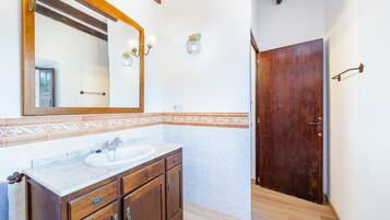 A bathroom with a wooden vanity, a large mirror, and a tiled backsplash.