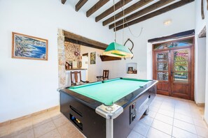 Una mesa de billar en una habitación con pared de piedra, vigas de madera en el techo y una puerta con paneles de vidrio.