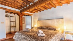 A bedroom with a wooden ceiling, a patterned bedspread, two pillows, and a bedside table with a lamp. - Libeccio Urban Suite by Pleiades Home (Livorno)