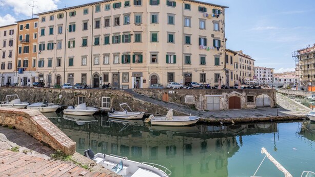 A waterfront building with multiple balconies and a canal with boats. - Libeccio Urban Suite by Pleiades Home (Livorno)