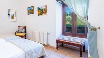 A bedroom with a bed, a chair, a bench, a radiator, and a window with curtains.