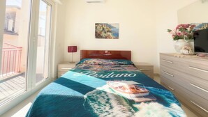 A bedroom with a bed, a nightstand, a lamp, a dresser, a TV, a painting, and a window with a balcony. - Sorrento Coast - Casa Raffaella : spacious panoramic penthouse (Meta)
