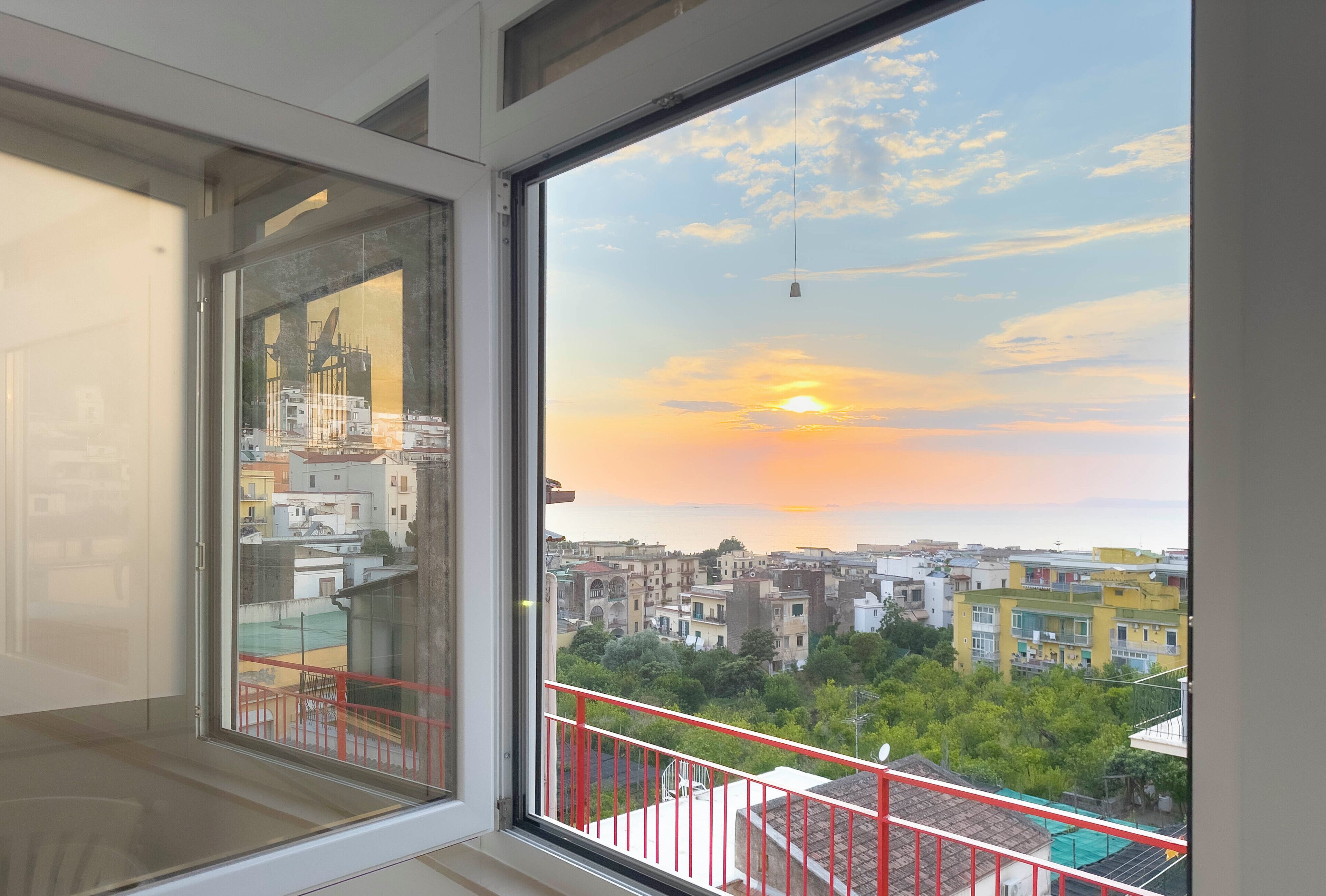 Quarto com uma janela ampla que oferece vista para a paisagem urbana ao pôr do sol.
