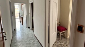A hallway with a tiled floor, white walls, and a door leading to a room with a bed and a red pillow. - Sorrento Coast - Casa Raffaella : spacious panoramic penthouse (Meta)