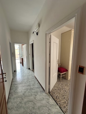 A hallway with a tiled floor, white walls, and a door leading to a room with a bed and a red pillow.