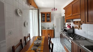 A kitchen with wooden cabinets, a dining table with chairs, a stove, and a microwave. - Sorrento Coast - Casa Raffaella : spacious panoramic penthouse (Meta)