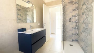Un bagno moderno con uno specchio grande, un mobile lavabo blu scuro, una doccia con piastrelle decorate e una porta che conduce in un'altra stanza.