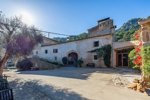 A rustic building with an arched entrance, a paved courtyard, and a dog lying on the ground.