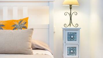 A bed with a white headboard, a yellow pillow, a beige pillow, and a bedside table with a lamp and two drawers.