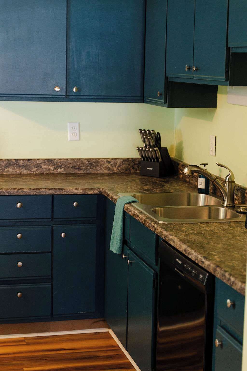 A kitchen with dark blue cabinets, a granite countertop, a stainless steel sink, and a dishwasher.