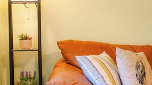 Ein gemütliches Wohnzimmer mit einem Ledersofa, einem gestreiften Kissen und einem kleinen Regal mit Pflanzen.