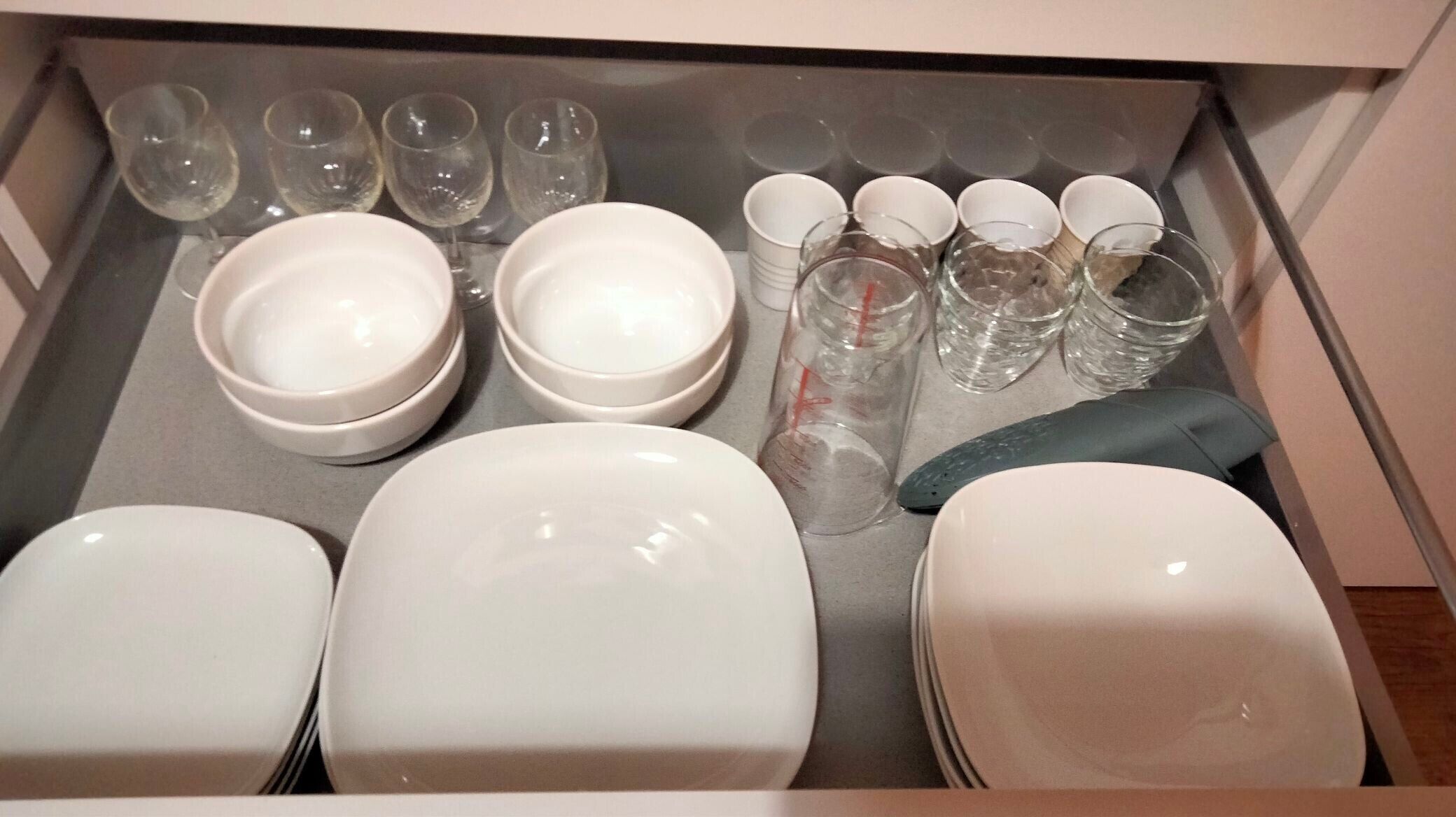 Un cajón con platos blancos, tazones y vasos transparentes.