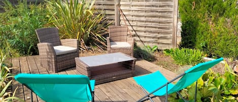 Una terraza de madera con mobiliario de mimbre, incluyendo dos sillas y una mesa.