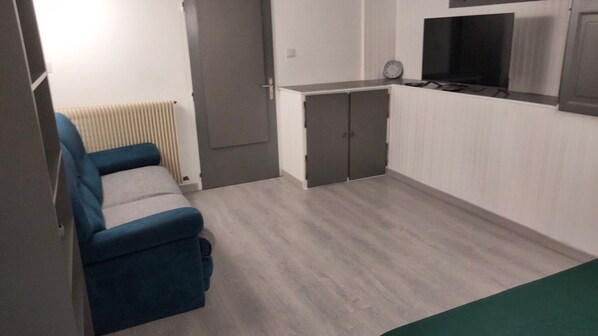A compact kitchen with a built-in oven, a small dining area with a blue chair, and a radiator.