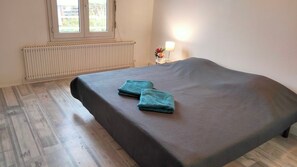 A room with a bed, a radiator, a window, and a nightstand with a lamp and flowers.