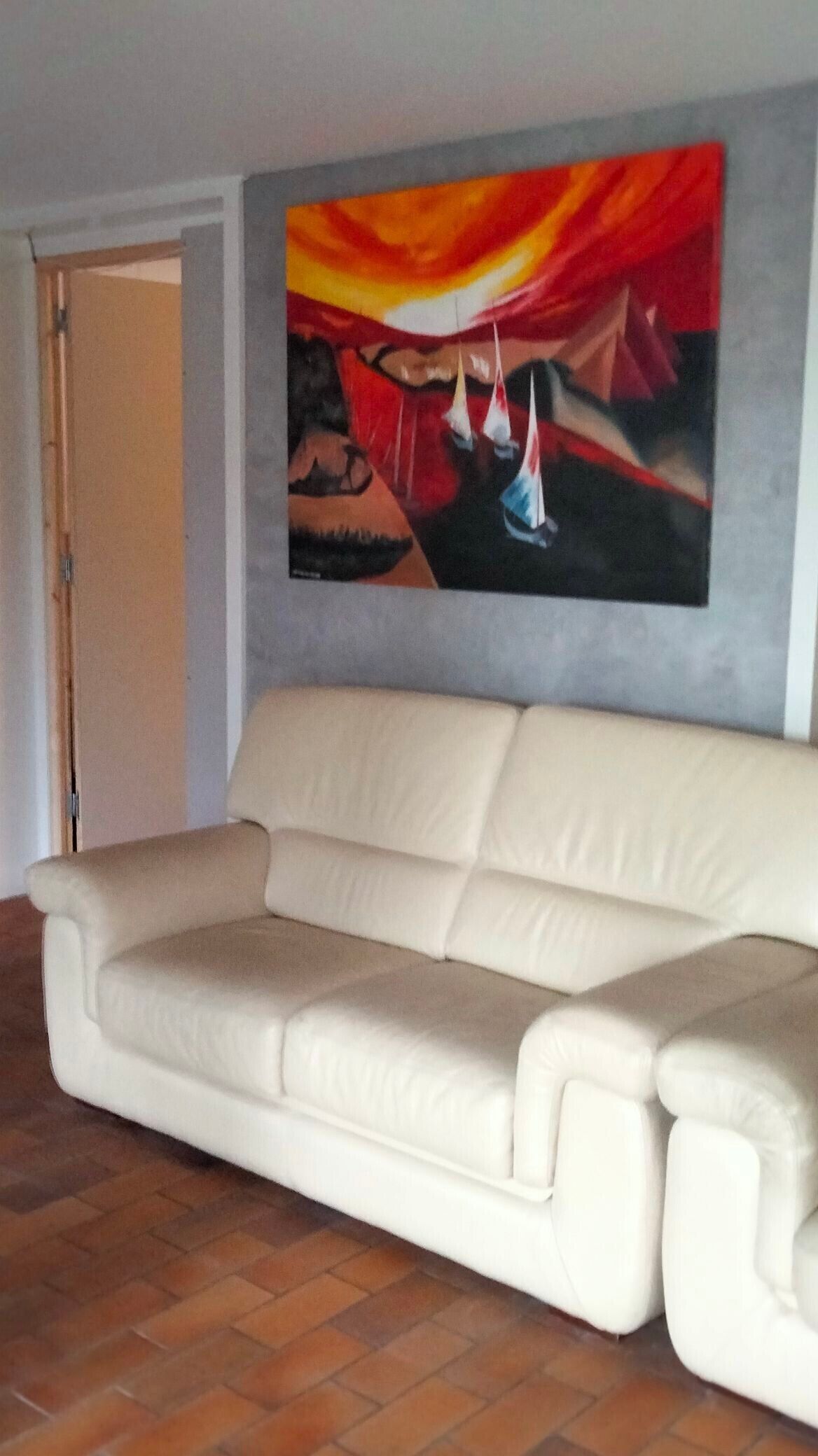 Un canapé beige dans une pièce dont le sol est carrelé et où l’on peut voir un tableau représentant des voiliers accroché au mur.