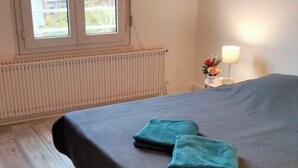 Ein Zimmer mit Bett, Fenster, Heizkörper und Nachttisch mit Lampe.