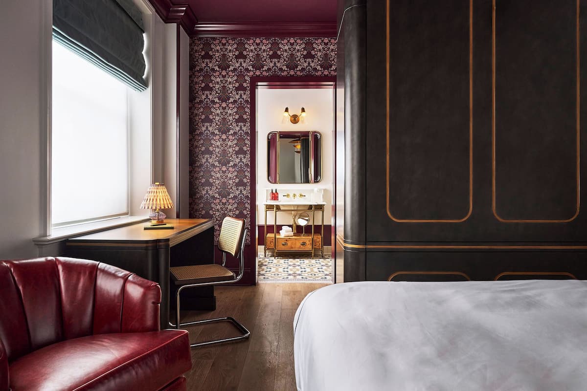 Una habitación de hotel con una cama grande, un escritorio con lámpara, una silla, un tocador con espejo y un armario.