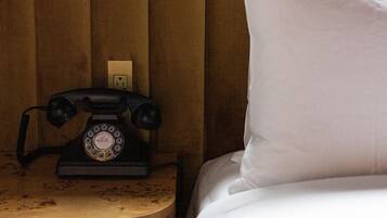 Een bed met een wit kussen en een oude draaischijf telefoon op een houten nachtkastje.