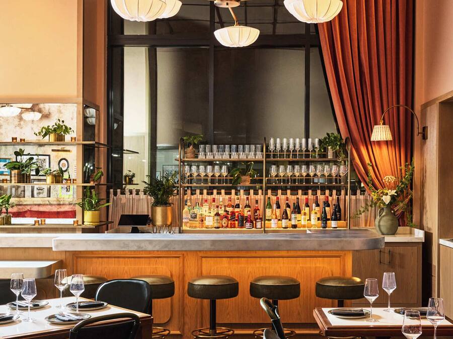 Un área de bar con diversas opciones de asiento, una barra bien surtida y un ventanal con cortinas.