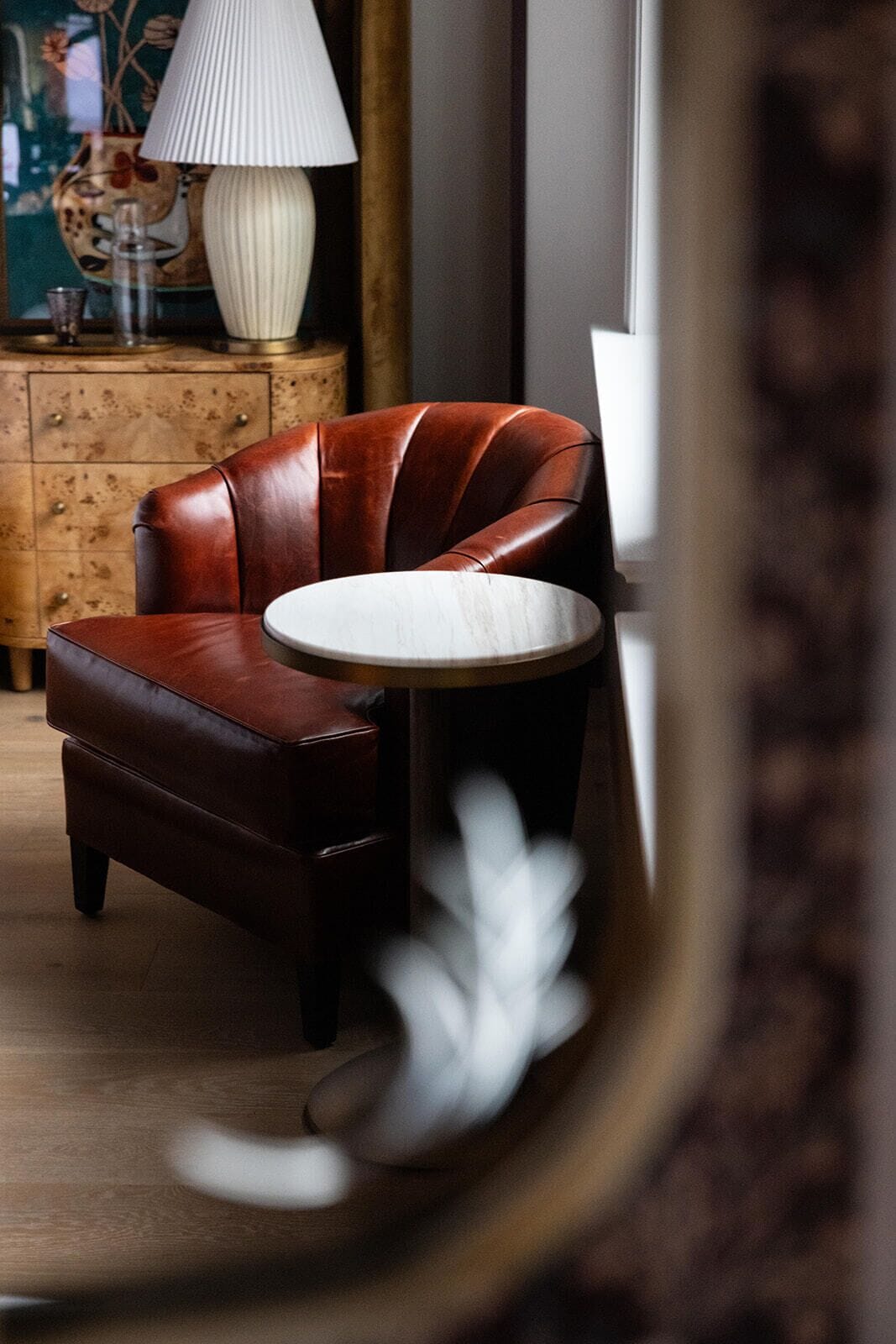 A leather armchair with a round table beside it, a lamp, and a decorative vase on a wooden cabinet.