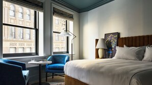 Una camera d'albergo con un letto grande, una poltrona blu, un tavolino e una lampada.